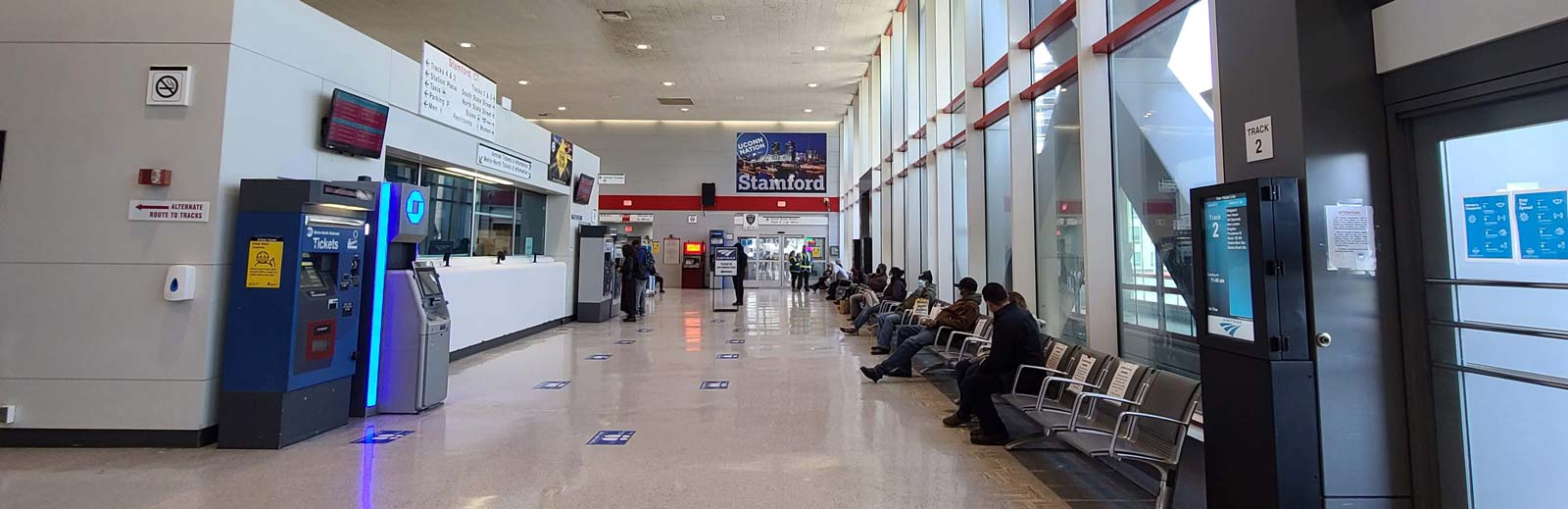 Interior concourse area view of ticket purchasing windows, people seated in waiting area.