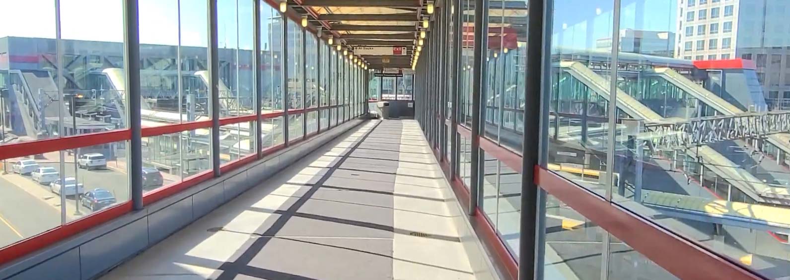 Glass window-enclosed elevated walkway spanning a road.